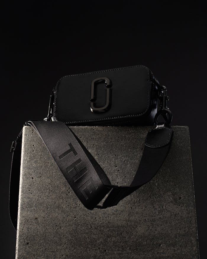 Elegant black handbag displayed on a concrete pedestal in a dark, modern setting.